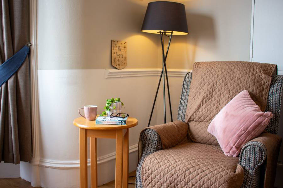 Inviting reading nook in the care home lounge. A comfortable chair with a side table and lamp creates a cosy atmosphere perfect for curling up with a book.