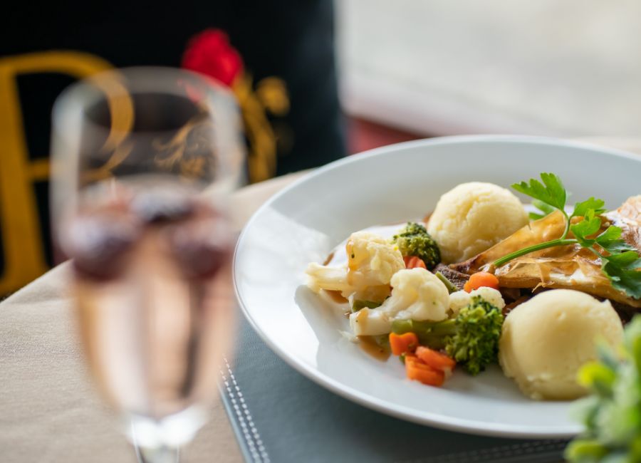 a prosecco glass with fresh fruit in the foreground with a homemade meal of vegetables, mashed potato, and steak pie in the background 