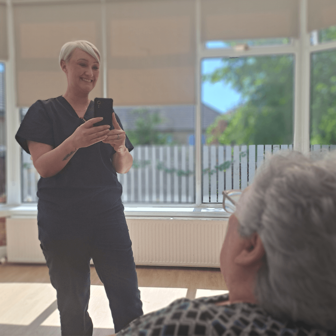A nurse is completing a painchek assessment on a resident. She is standing, holding the device with the camera looking at the residents face