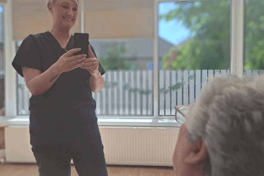 A nurse is completing a painchek assessment on a resident. She is standing, holding the device with the camera looking at the residents face