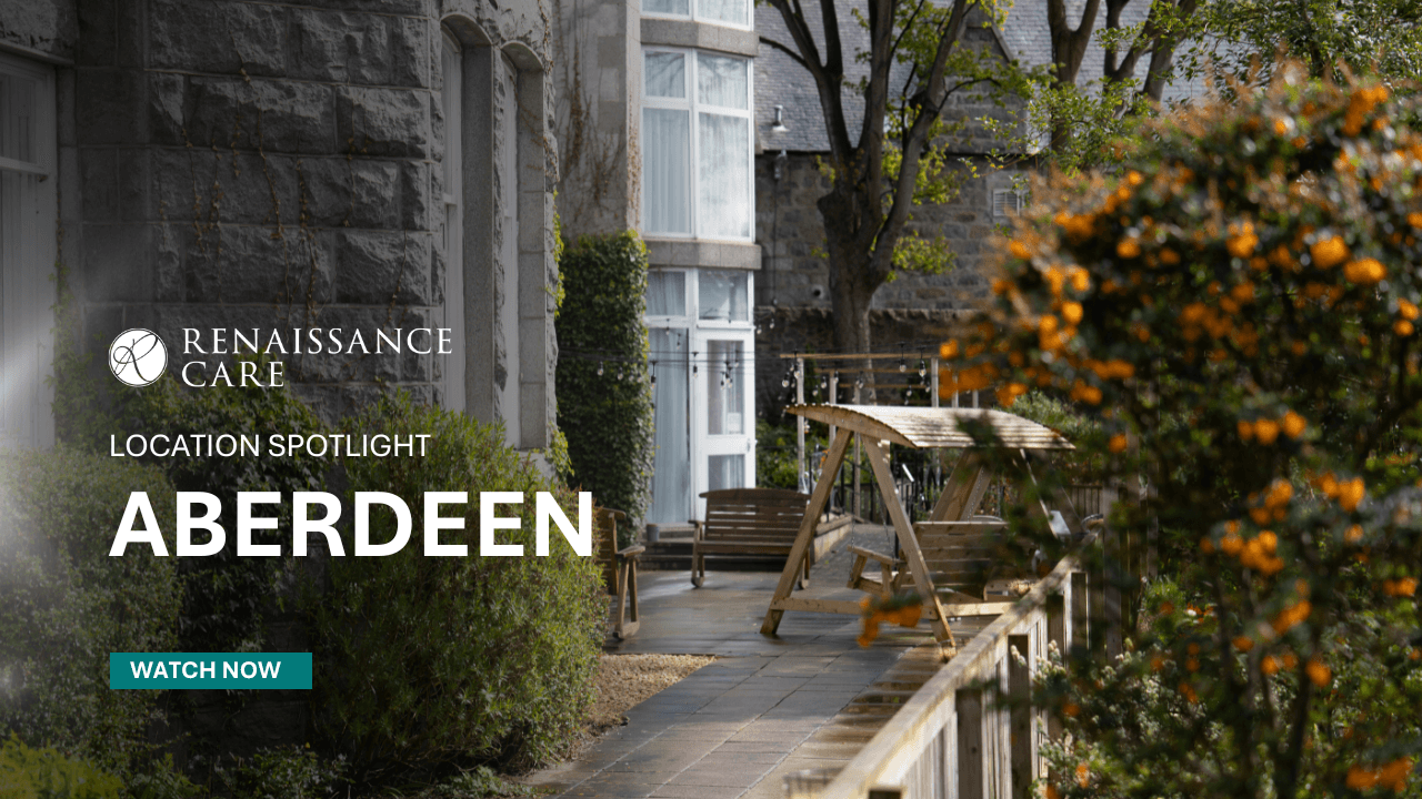 An autumnal garden with various bench seating and large grey granite building. A stone pathway and colourful shrubbery.  