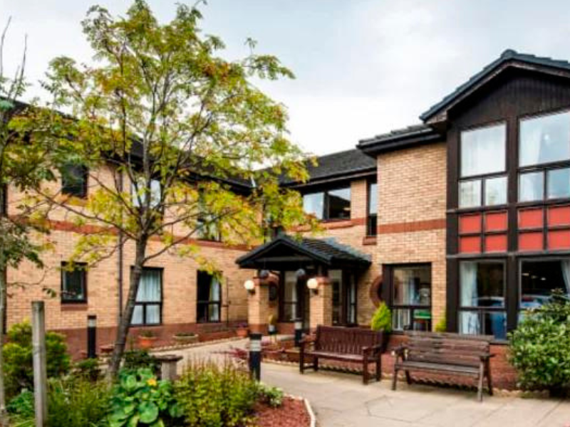 Orange and red bricked exterior of Whitecraigs Care Home. There are seating areas and greenery present throughout