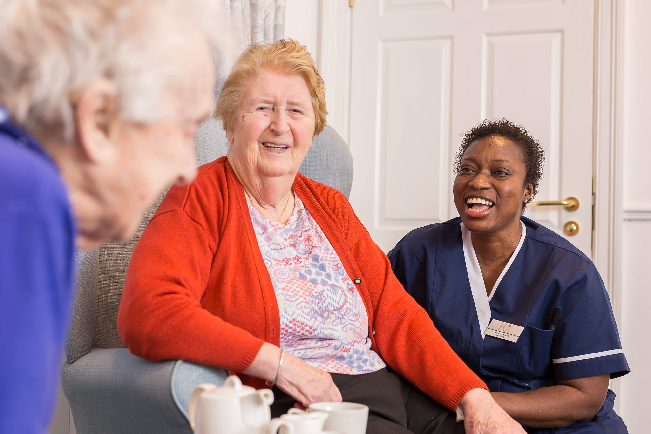 Residents enjoying a cup of tea and conversation with a staff member in the bright communal lounge.