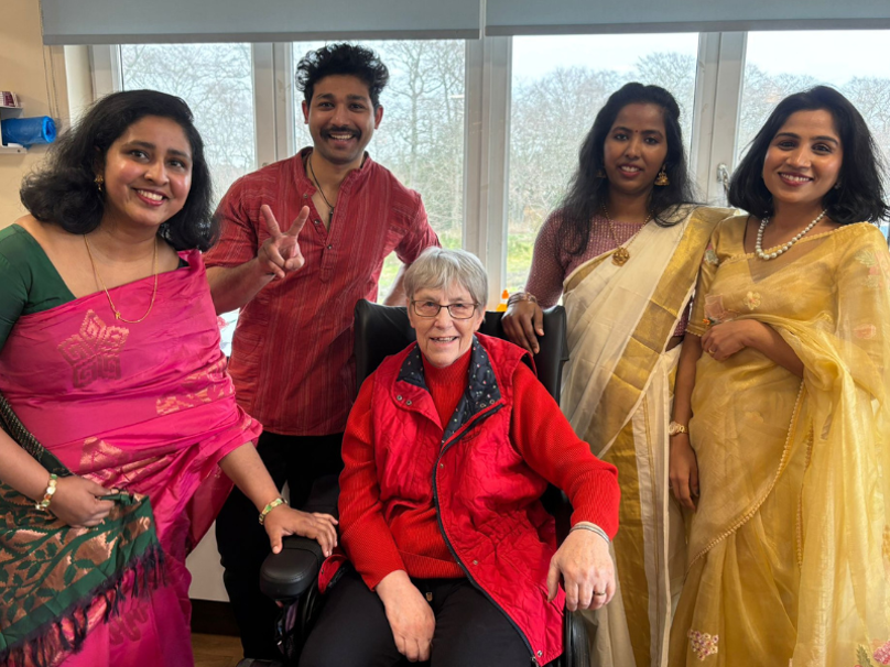 A collection of care home staff stand around a care home resident. The staff are showcasing their native dress as part of the homes fashion show