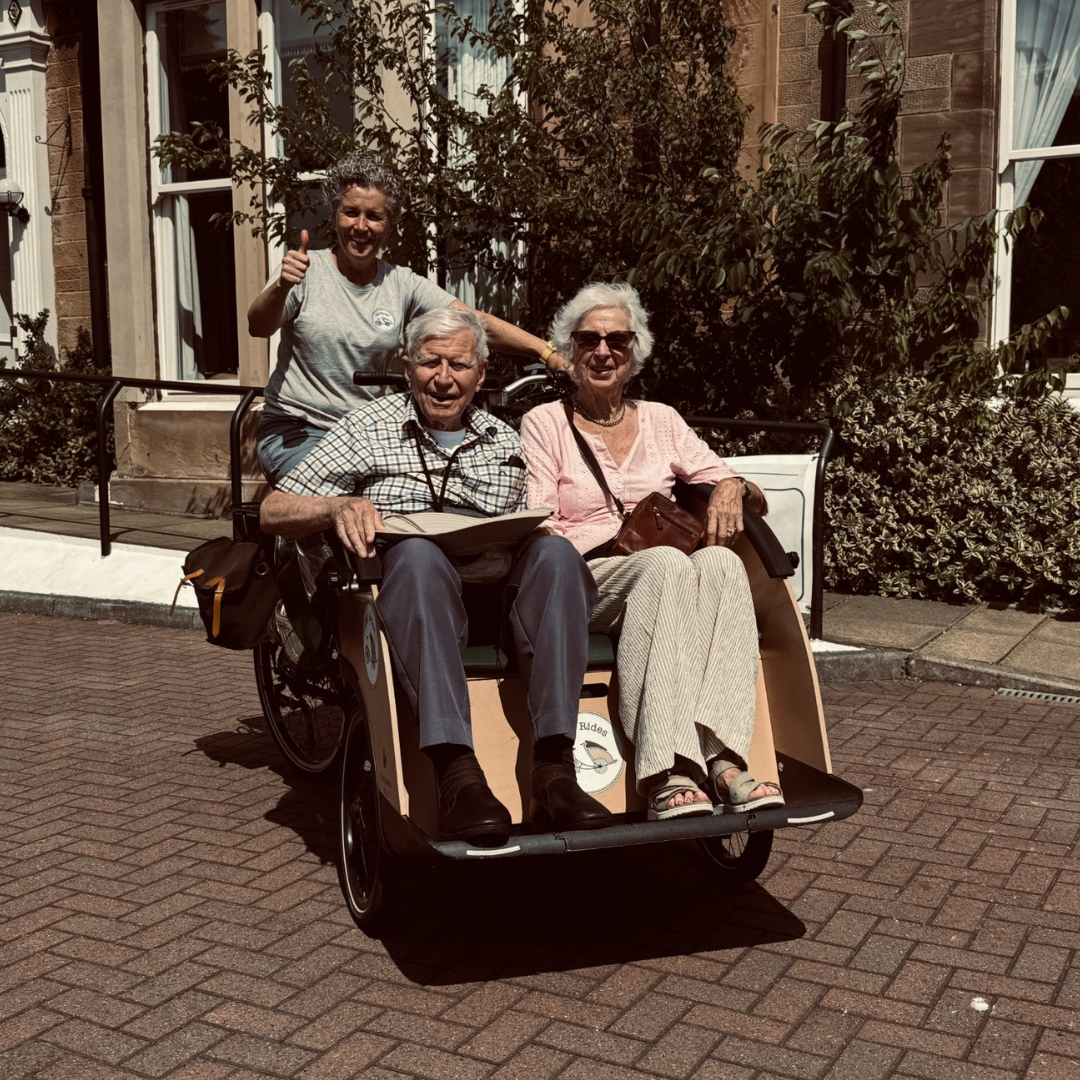 Two residents sit in a trishaw carriage in front of the care home as the operator prepares to cycle them around Edinburgh