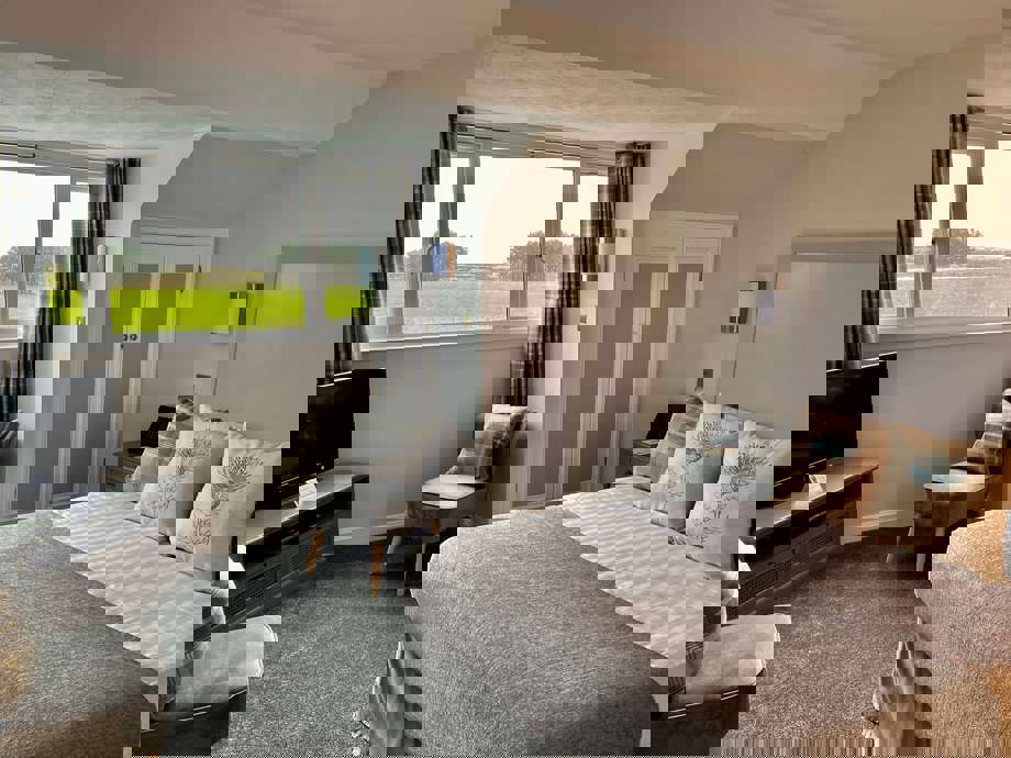 Malin Court Respite Room : A bedroom set up with bed, chair, TV unit, and window looking out into the garden 