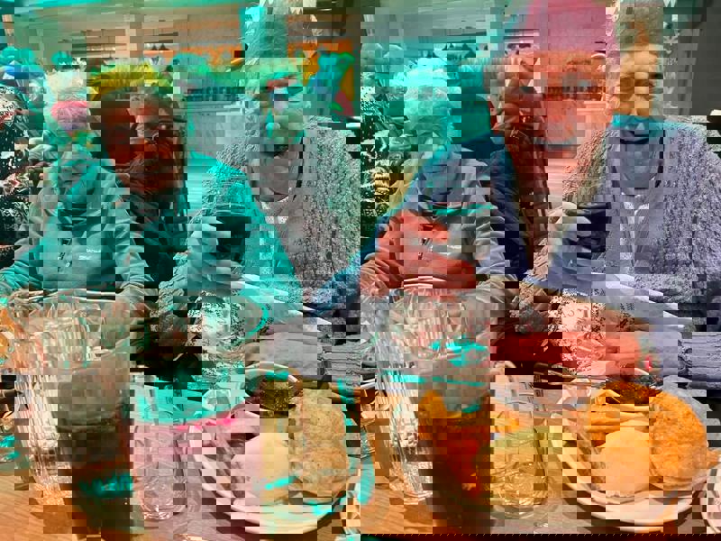 Care Home residents enjoy a Christmas meal together, one lifts her glass of wine up in a 'cheers!' motion