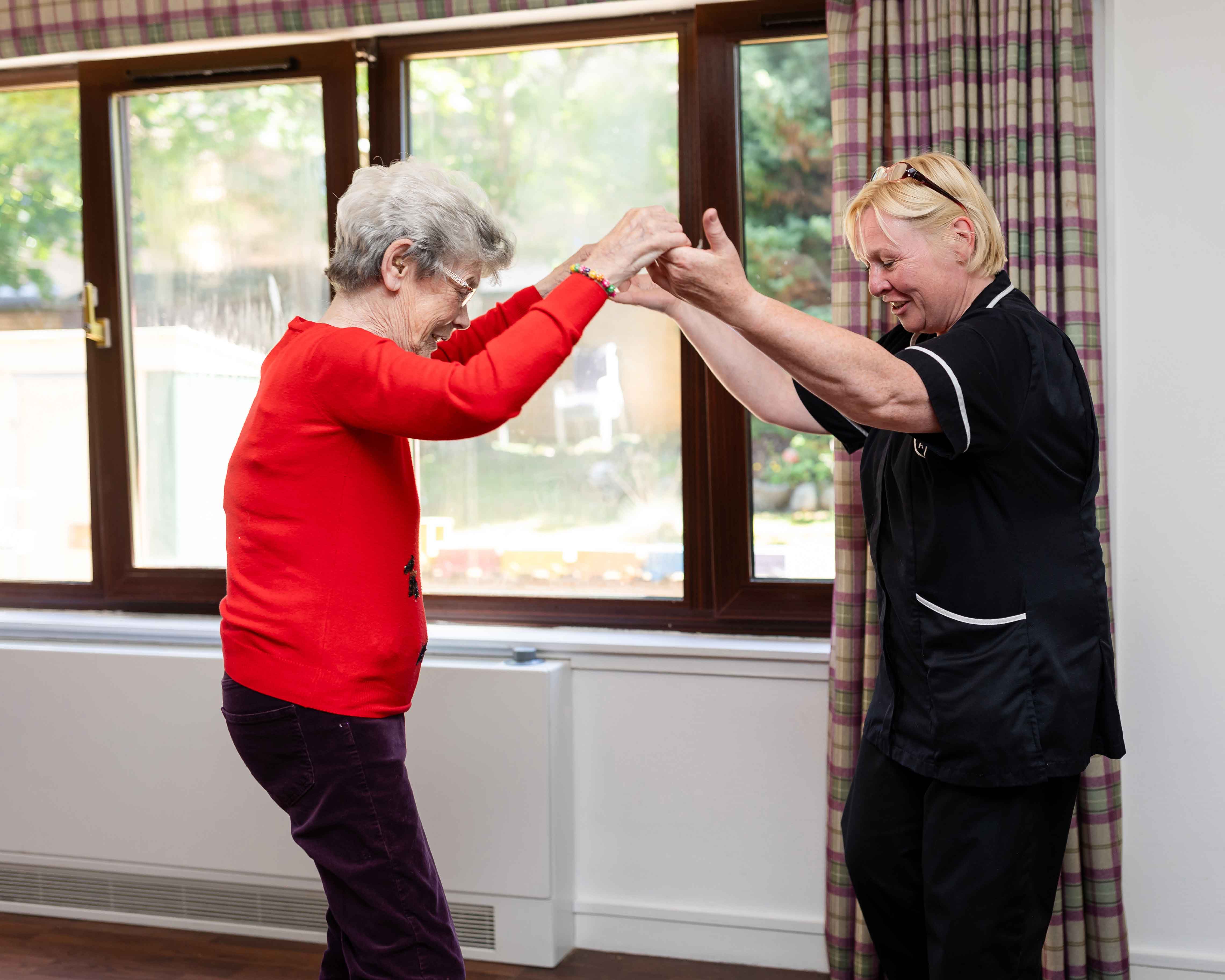 A staff member and resident enthusiastically dance together, with their arms in the air 