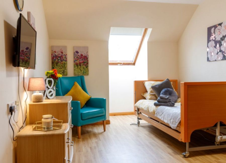 A bedroom set up with wooden furniture, brightly coloured armchair, and various artworks making it look cosy and inviting