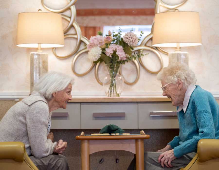two woman sit opposite each other engaging in a game of scrabble 