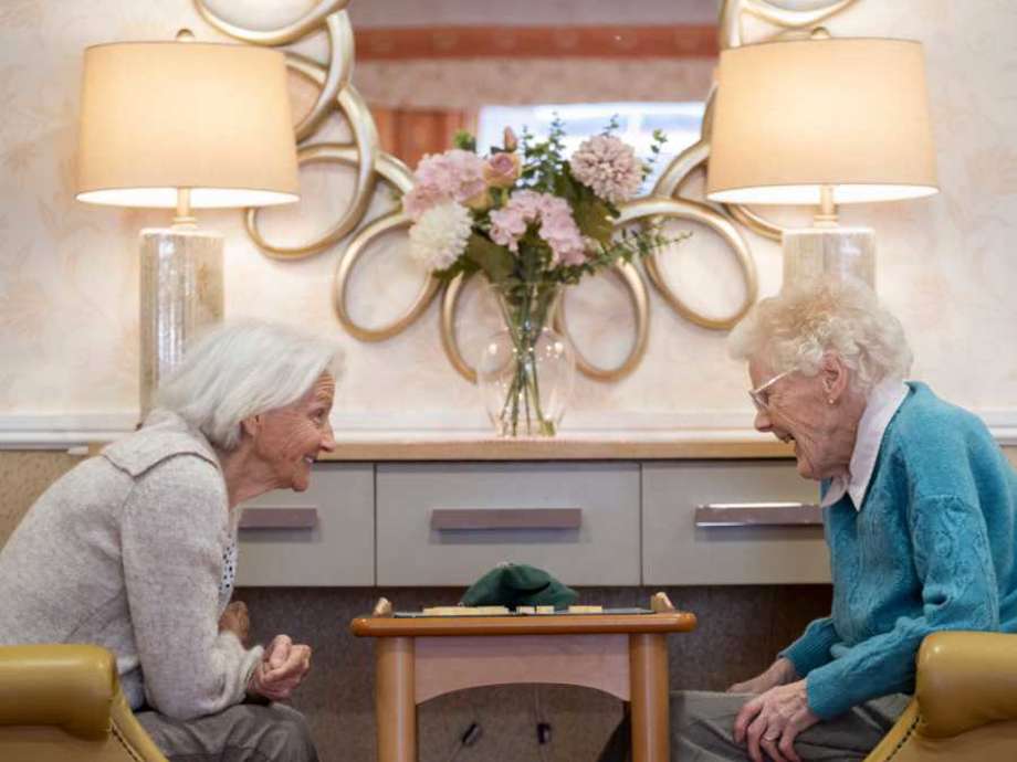 two woman sit opposite each other engaging in a game of scrabble