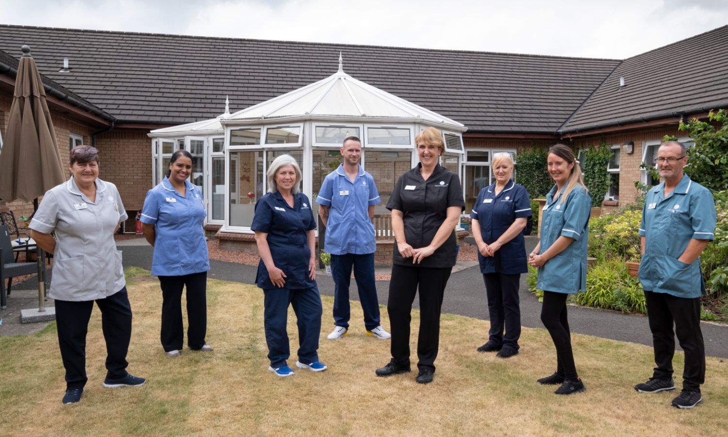 8 staff members stand outside the care homes conservatory surrounded by garden space