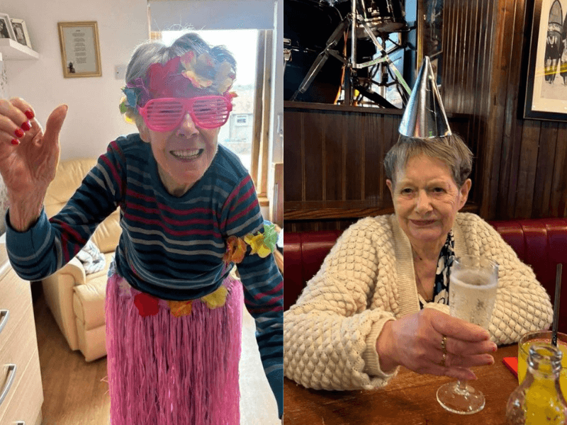 Resident Margaret stands on the left hand side ready to party, she is colourful in her lei and skirt. On the right, we have Carol who has a cream cardigan on, a glass of prosecco in one hand, and a party hat. 