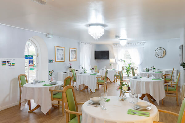 Sunlight floods a spacious dining room with tables and chairs arranged for a meal