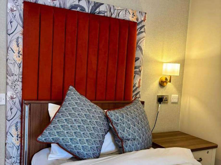 Modern bed with a burnt orange and floral headboard, two geometric cushions, and white bedding.