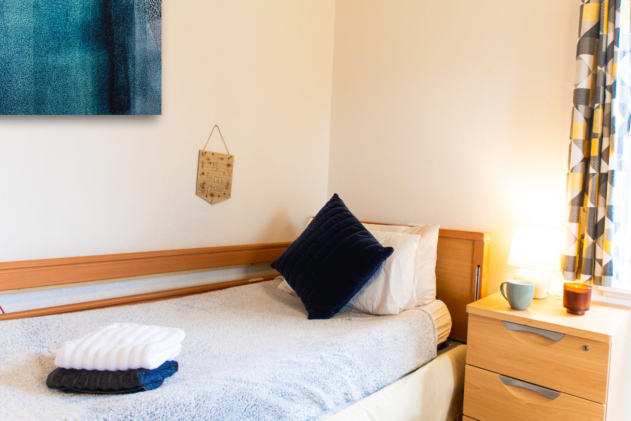Care home bedroom with a wooden bed and side table. Navy blue accents and artwork personalise the space.