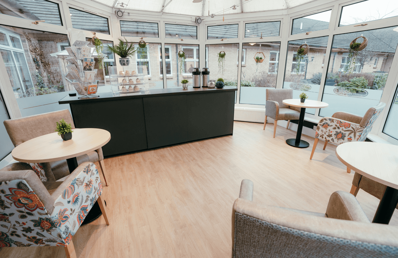 A bright and modern conservatory and cafe space with a large black servery and wooden tables with paisley pattern armchairs