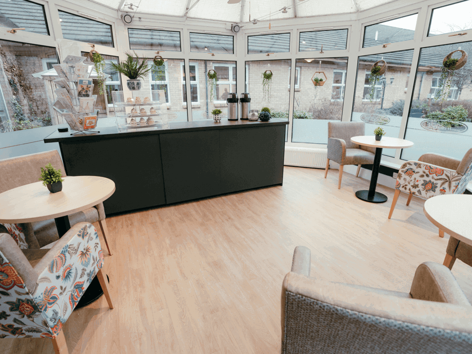 A bright and modern conservatory and cafe space with a large black servery and wooden tables with paisley pattern armchairs
