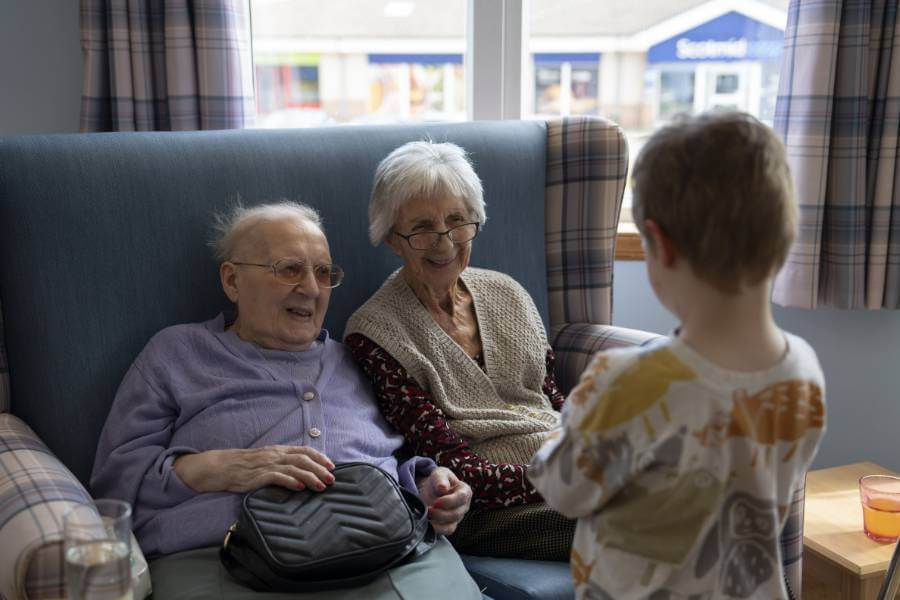 Two care home residents share a warm smile with a visiting nursery child