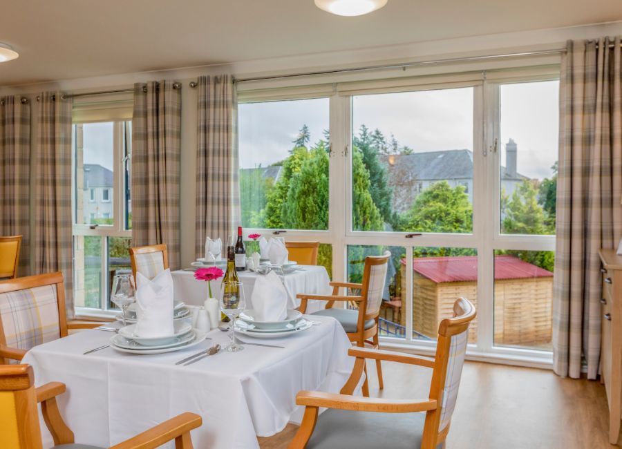 Multiple tables and chairs make up this dining room, with napkins and tableware throughout, and overlooking the garden through large floor to ceiling windows