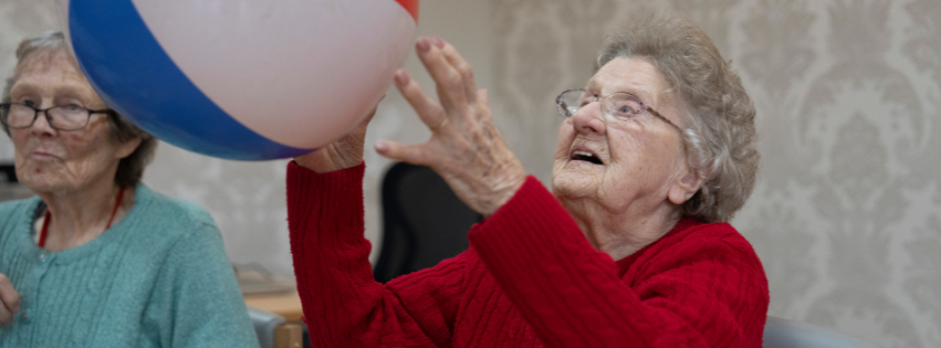 A woman in red knitwear hits a beach ball in an exercise class