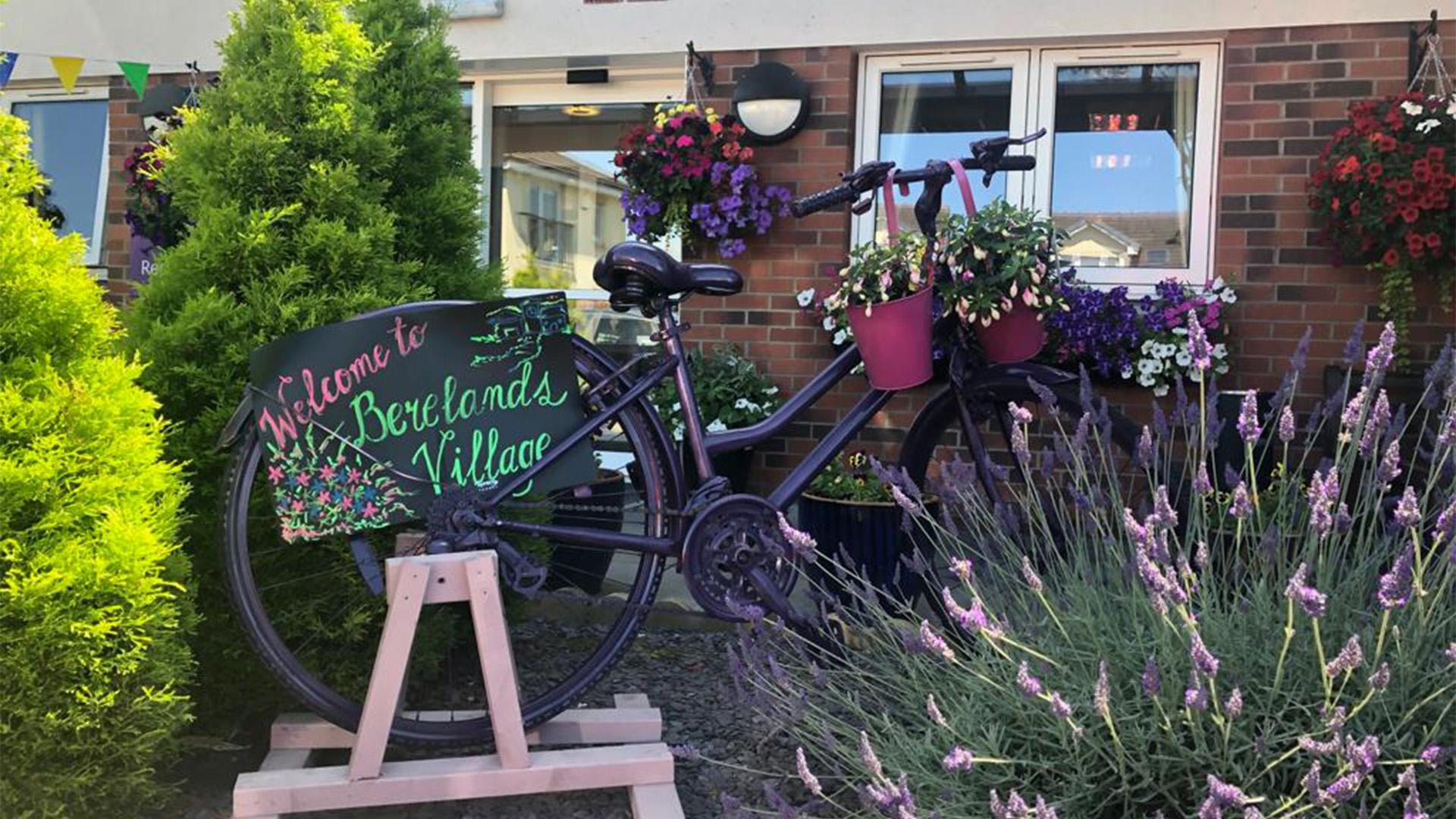 Berelands Village: A bike sits in amongst a garden area with a sign reading ' Welcome to Berelands Village ' 