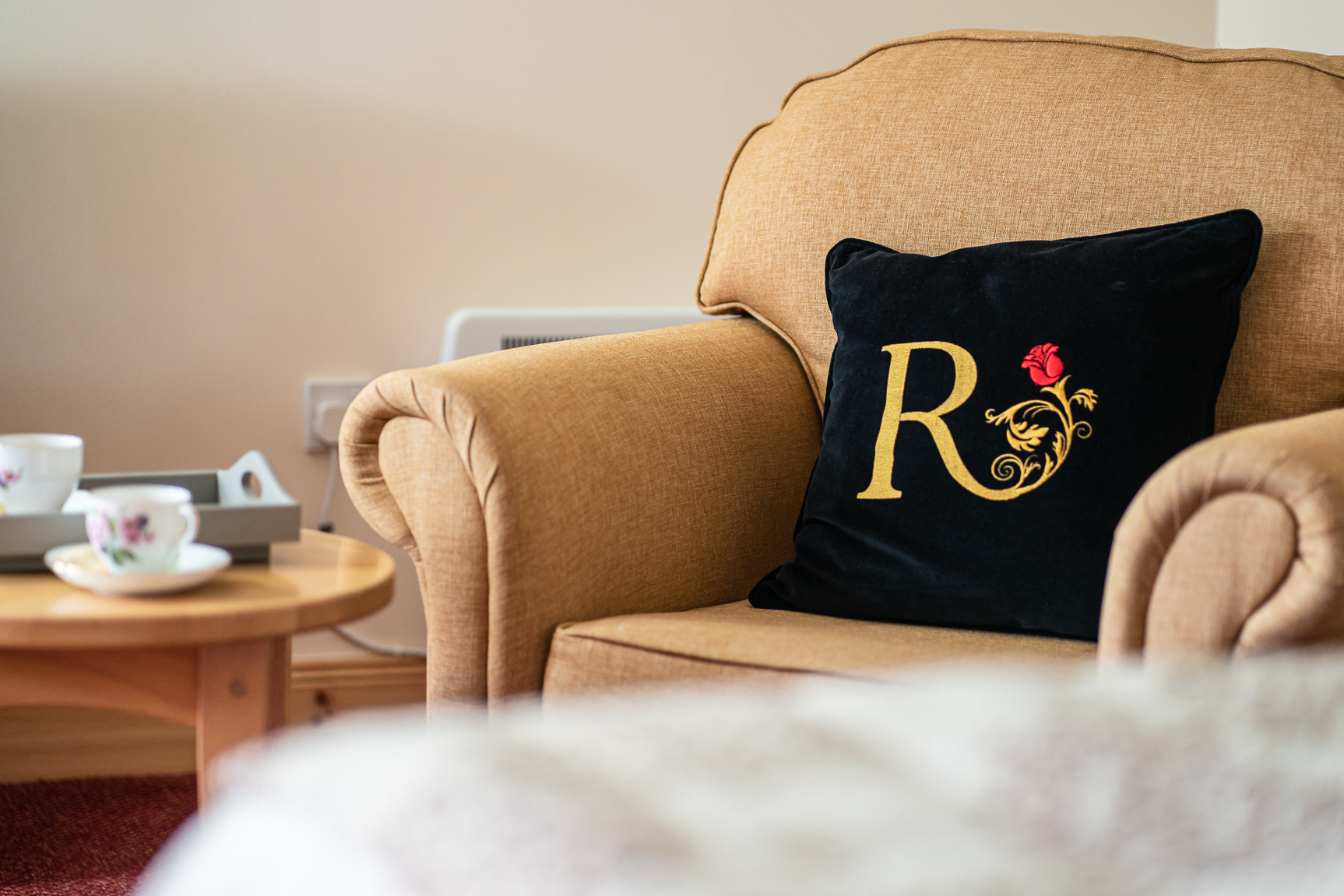 A chair with Renaissance At branded cushion, a golden R with a red rose, next to a table offering tea