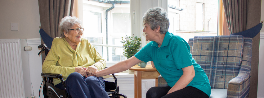 Wyndwell resident and staff member sitting together and smiling within the communal lounge 