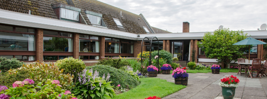 Malin Court exterior, a building with a red/brown brick facade and a vibrant flower garden.