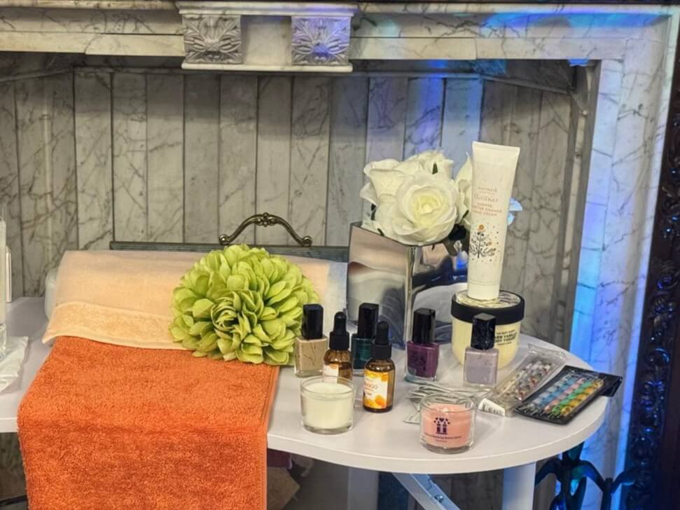 A selection of nail polishes and skin care sits on a white table alongside two orange coloured towels - ready for a namaste care session.