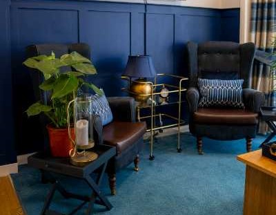 Sophisticated communal lounge featuring high-backed chairs and rich wood paneling. Homey plants and navy accents create a warm and inviting atmosphere