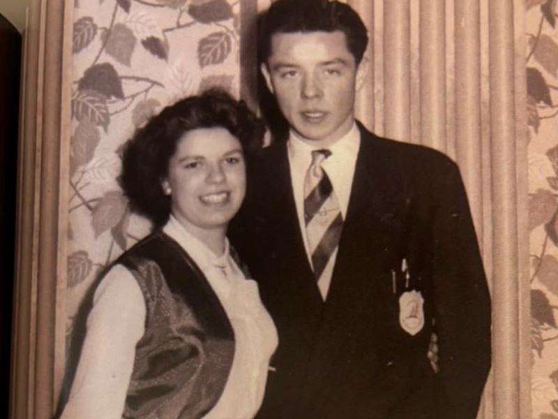 An old black and white photograph of a couple. They are smartly dressed and stand side by side. 