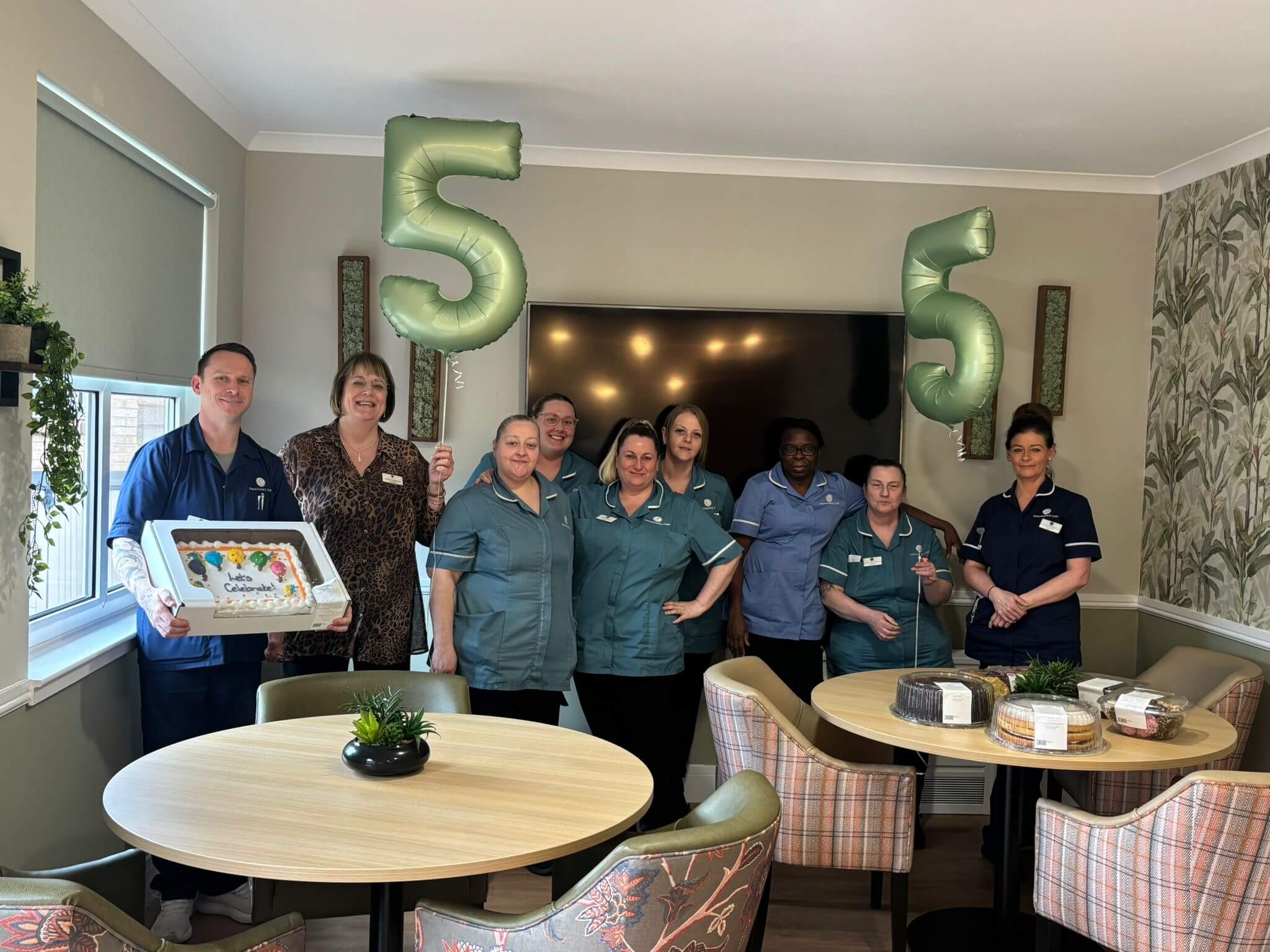 Members of the staff team stand proudly, with two '5' balloons and an assortment of cakes to celebrate the success of a recent inspection