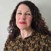 Headshot of care home manager, Tracey McMillan. She has curly brown hair, and is wearing a black blouse with mustard yellow floral detail 