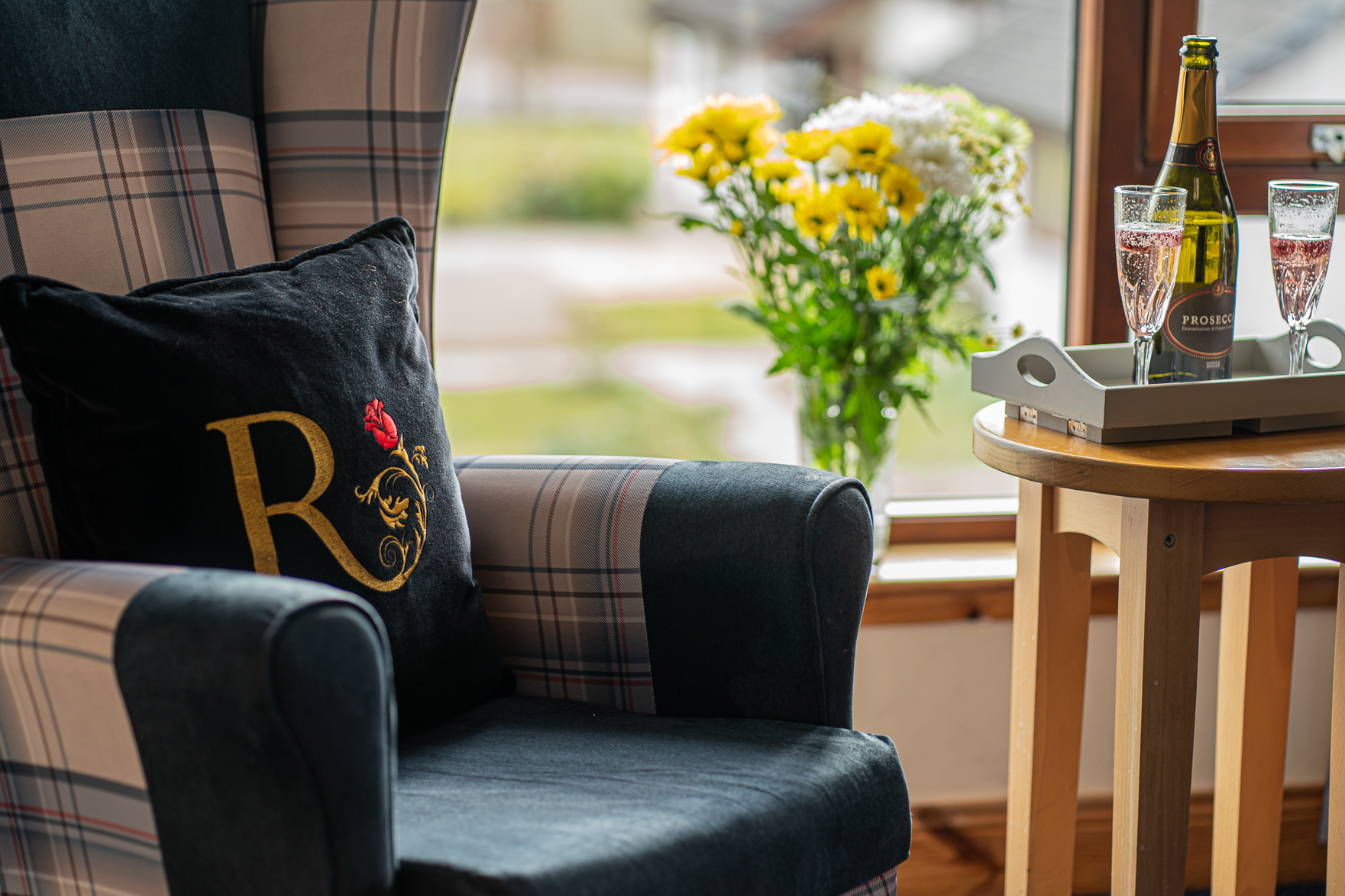 Close-up of a high-backed chair beside a window. Two flutes of prosecco rest on a nearby wooden table