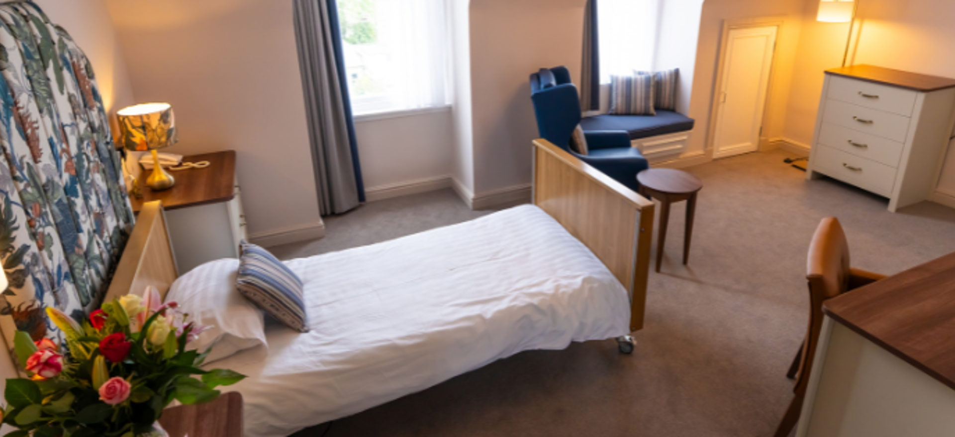 A bright and modern bedroom with lots of open space, a variety of furniture including a bed, desk, and armchair, and nice ambient lighting